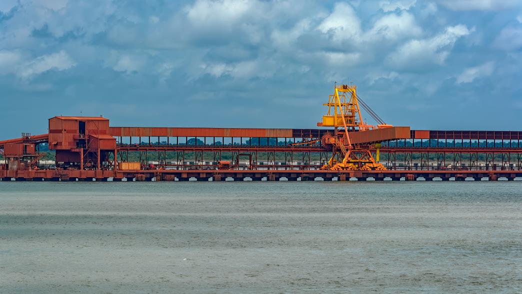 Outdoor industrial jetty at sea bank with incline large conveyor for transportation bauxite ore from mining shuttle trains to mini bulk carrier, Guinea